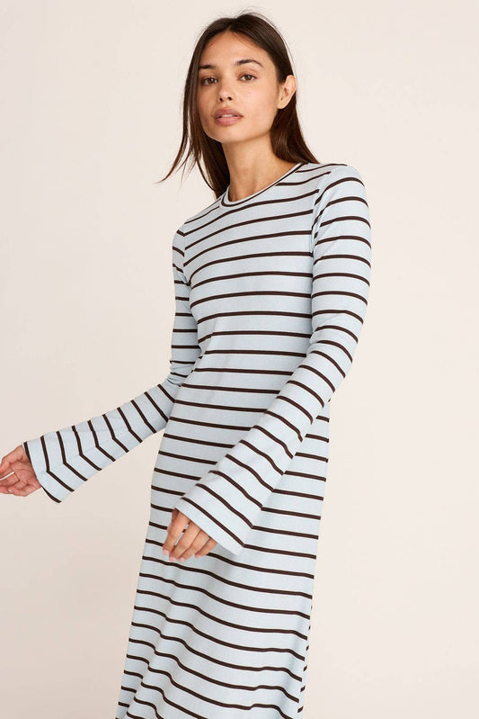 A woman modeling a long-sleeve knit dress with horizontal black stripes on a white background, photographed against a plain light beige studio backdrop.