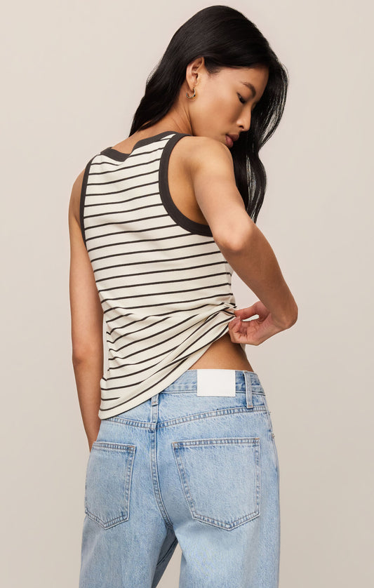 Woman wearing a striped tank top and jeans against a plain background