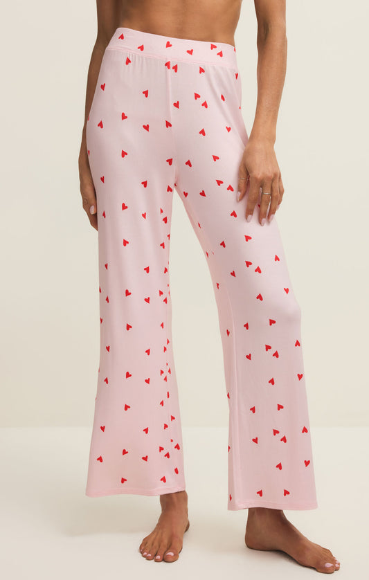 Pink pajama pants with red heart pattern worn by a person on a white background