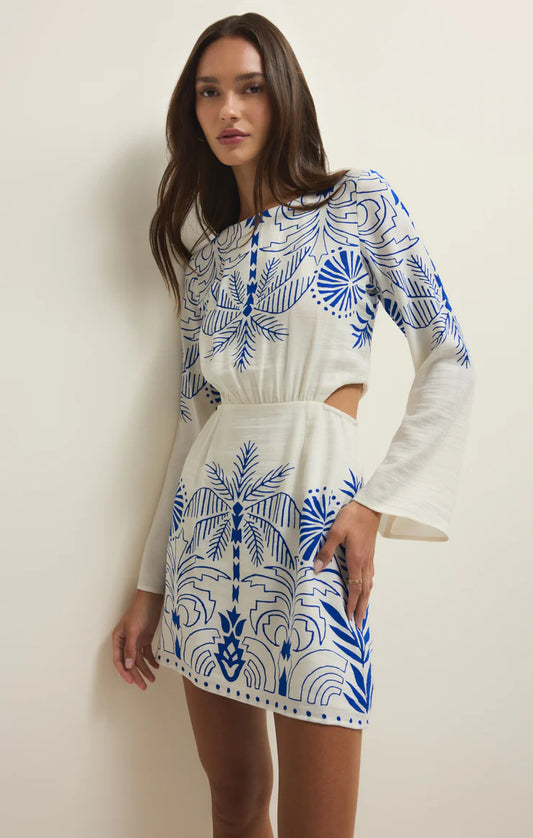 Woman wearing a white dress with blue patterns against a plain background