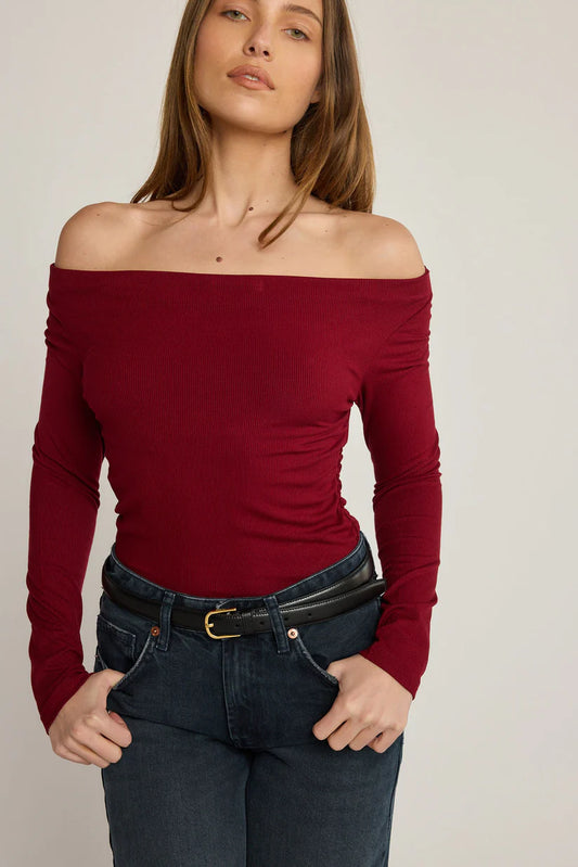 Woman wearing a red off-shoulder top and blue jeans against a plain background