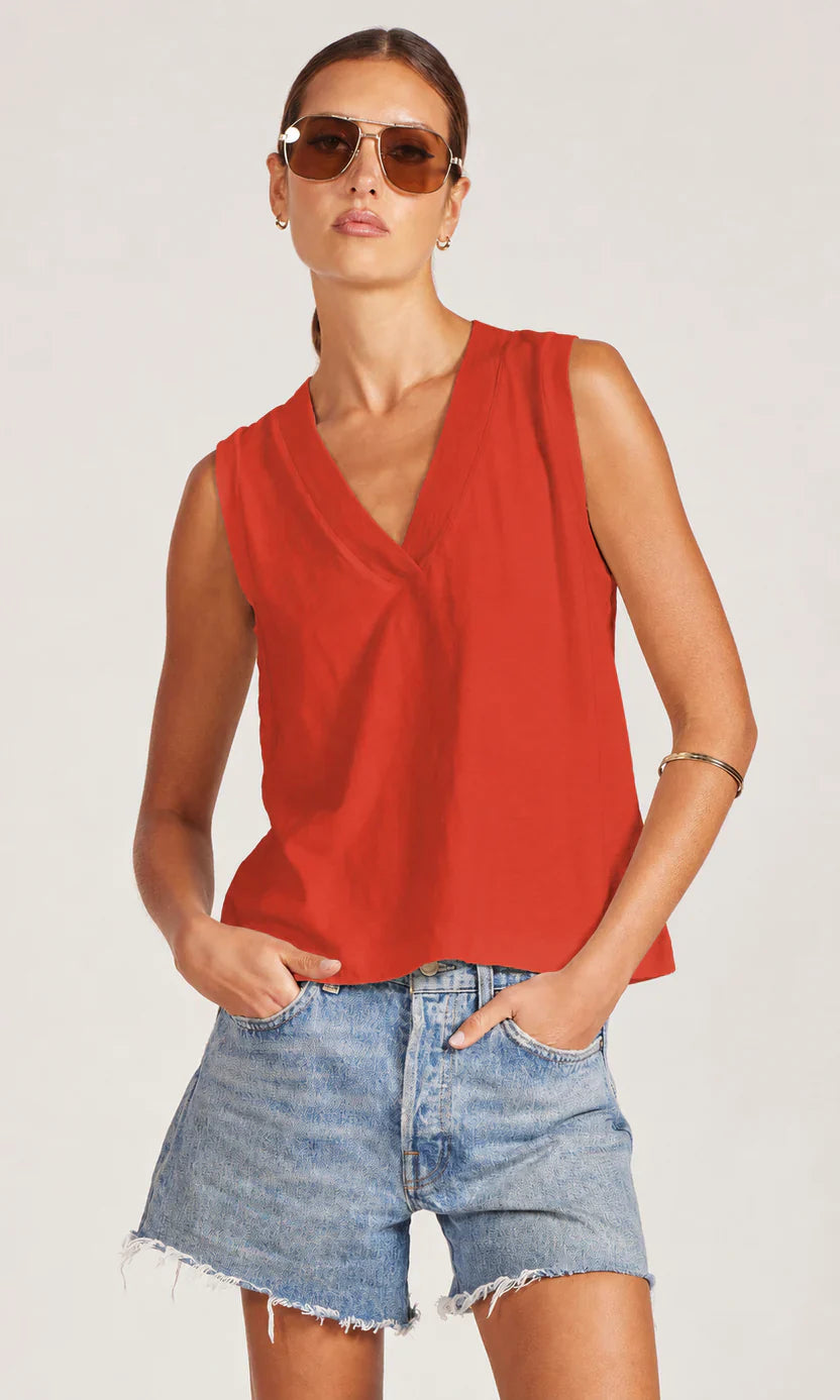 Woman wearing red tank and blue denim shorts on white background.