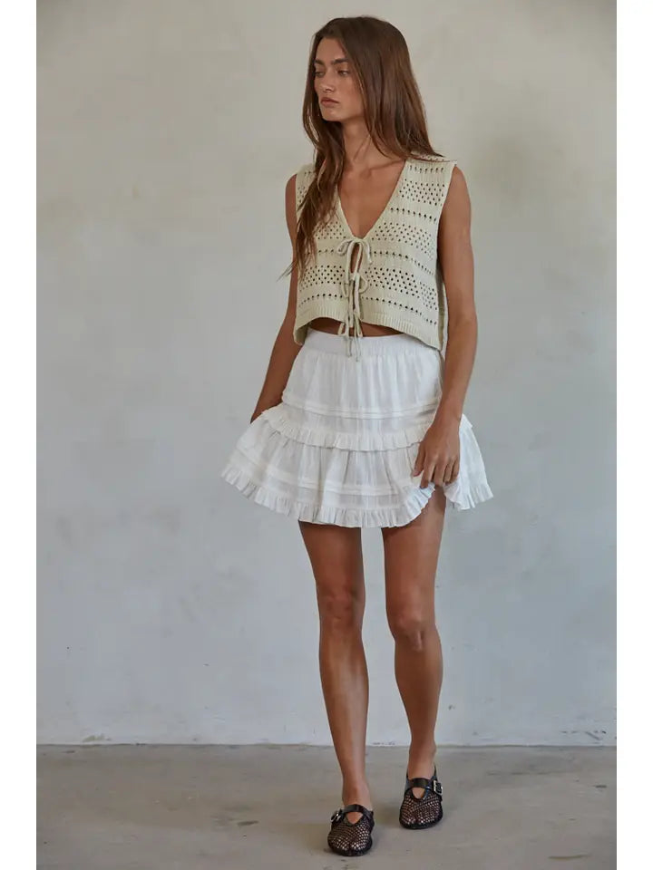 Woman wearing a light-colored sleeveless top and white skirt against a plain background