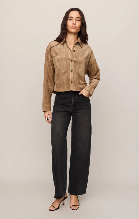 Woman in cropped brown jacket, white shirt, and black jeans on a white background.