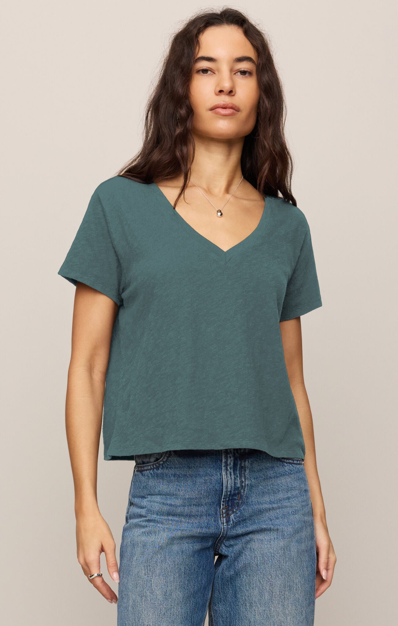 Woman wearing a teal V-neck t-shirt and blue jeans against a beige background