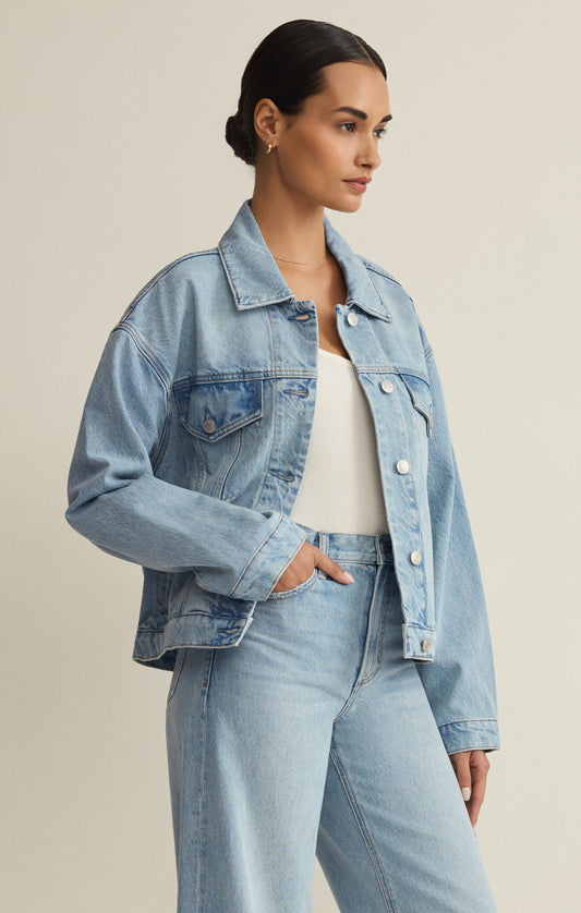 Woman wearing a light blue denim jacket and jeans on a beige background