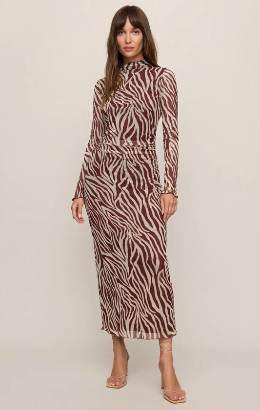 A woman modeling a long-sleeve mock-neck midi dress with a brown and beige zebra print, standing against a plain light beige studio background.