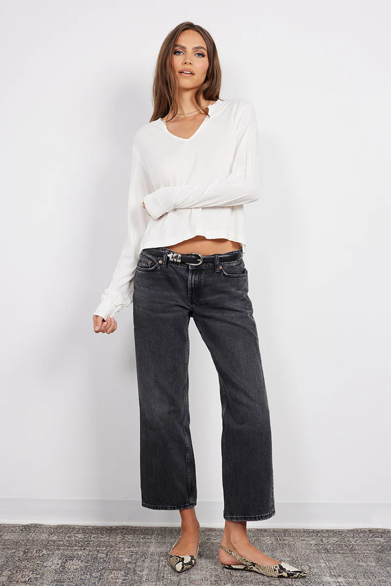 Woman wearing a white blouse and black jeans against a plain background