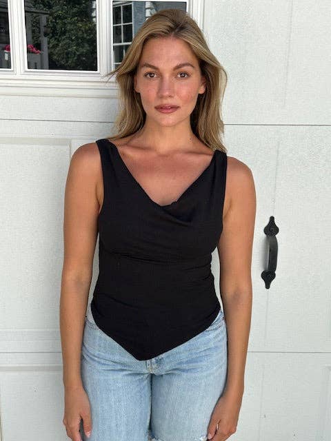 A woman wearing a black sleeveless cowl-neck tank top and light-wash blue jeans, standing in front of a white garage door.