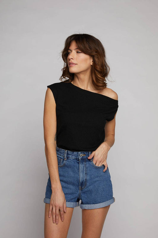 Woman wearing a black off-shoulder top and blue denim shorts on a plain background