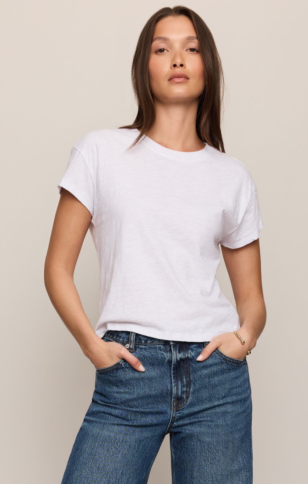 Woman wearing a plain white t-shirt and blue jeans against a beige background