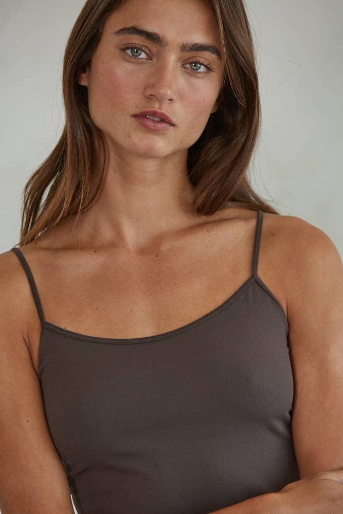 Woman wearing a brown spaghetti strap top against a neutral background