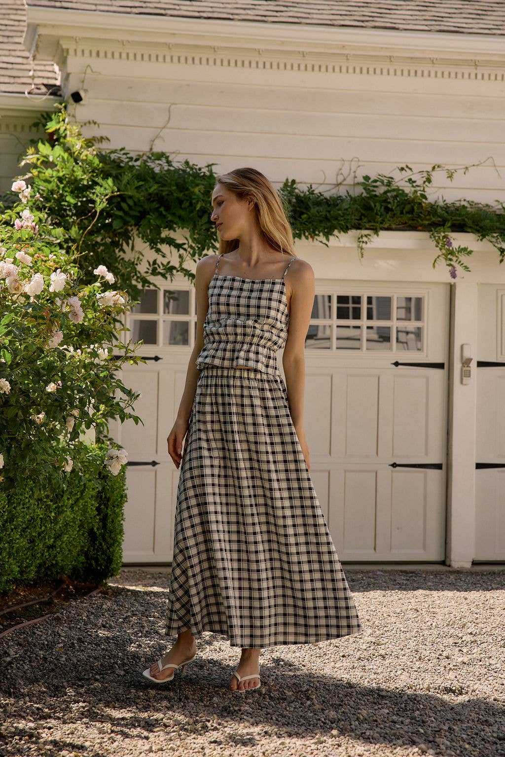 Woman in a checkered dress standing in front of a white building with greenery.