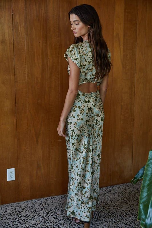 Woman wearing a floral dress standing against a wooden wall.