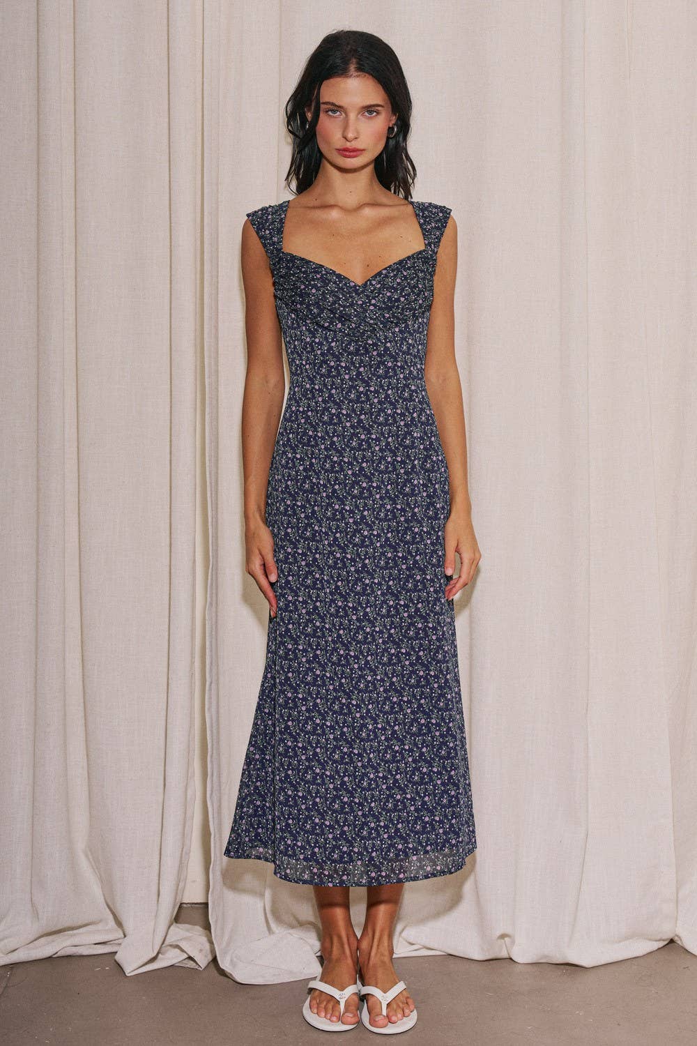 Woman wearing a navy floral dress against a white curtain background