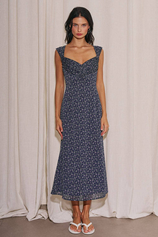Woman wearing a navy floral dress against a white curtain background