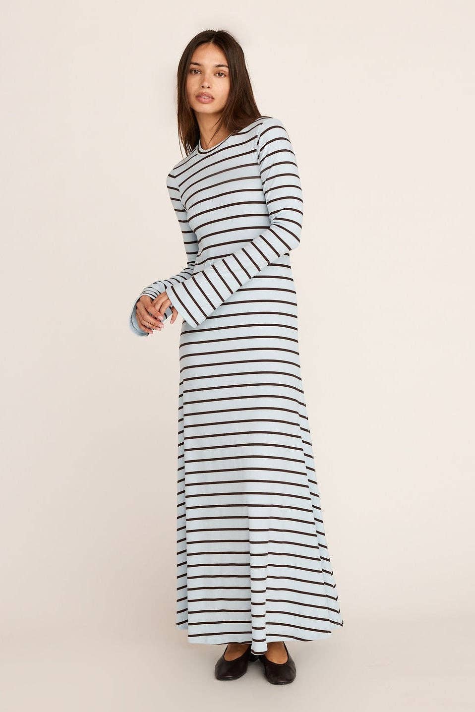 A woman modeling a long-sleeve maxi dress with horizontal navy and white stripes, standing against a plain off-white studio background.