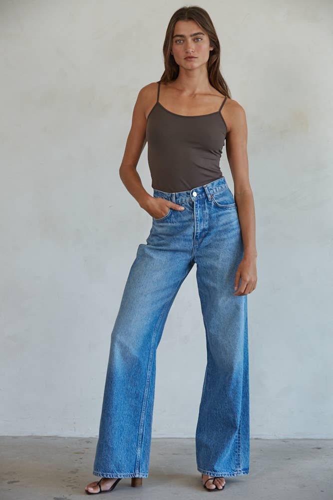 Woman wearing a brown tank top and blue jeans against a plain background