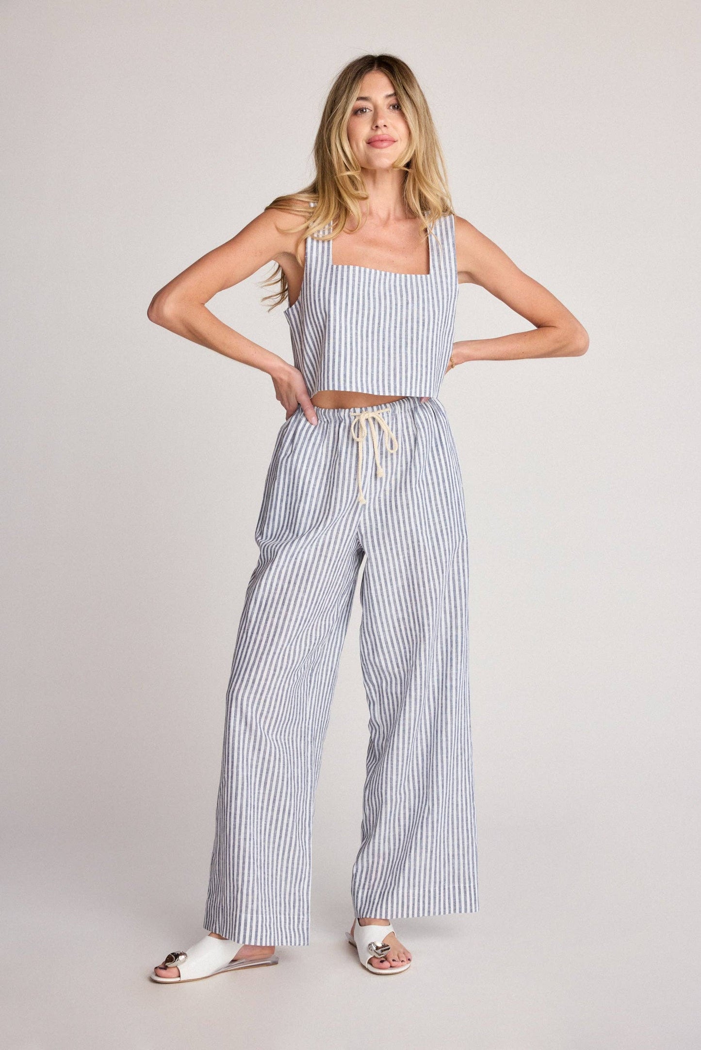 Woman wearing a striped tank top and wide-leg pants on a plain background