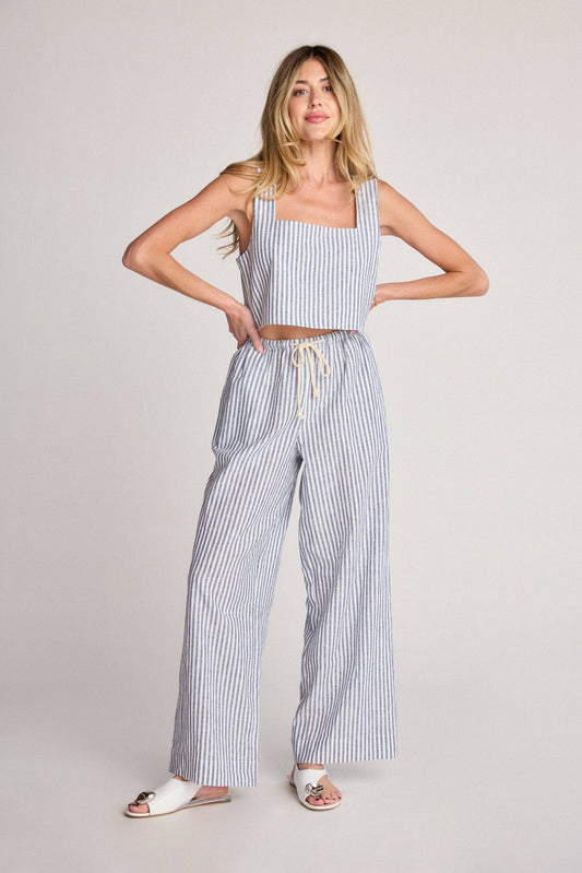 Woman wearing a striped tank top and wide-leg pants on a plain background
