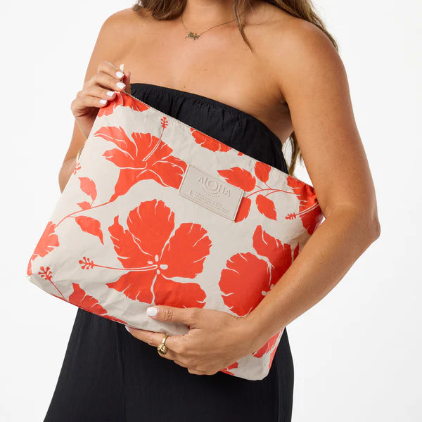 Woman holding a floral-patterned pouch with a visible brand logo on a white background