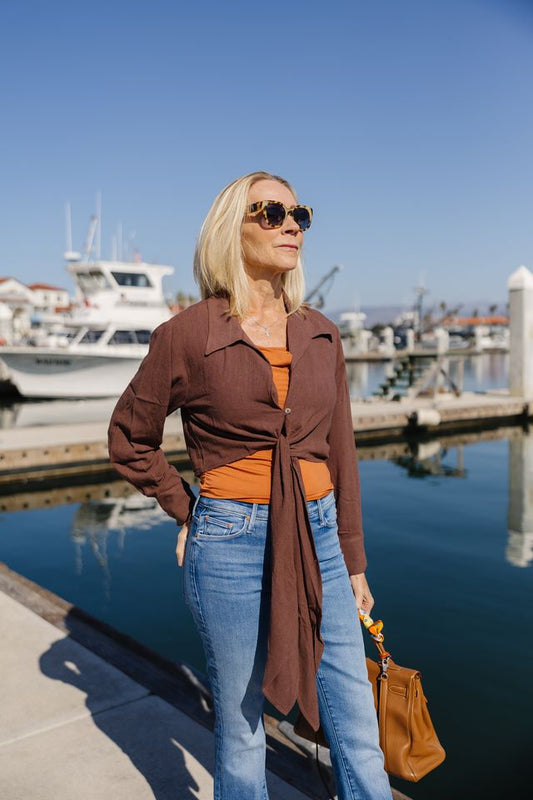 Woman in brown wrap top and blue jeans on a boat dock.