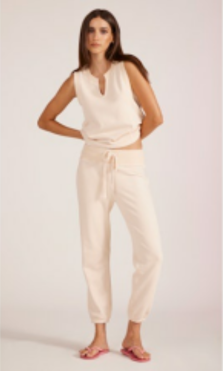 Woman wearing a cream sleeveless top and pants on a white background