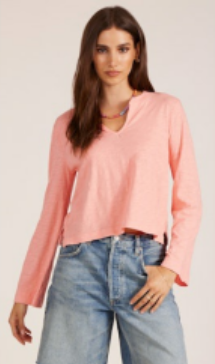 Woman wearing a pink long-sleeve top and blue jeans on a plain background