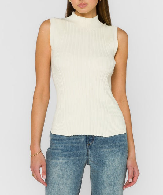 A woman wearing a ribbed sleeveless mock neck top in off-white, paired with blue jeans, against a light gray studio background.