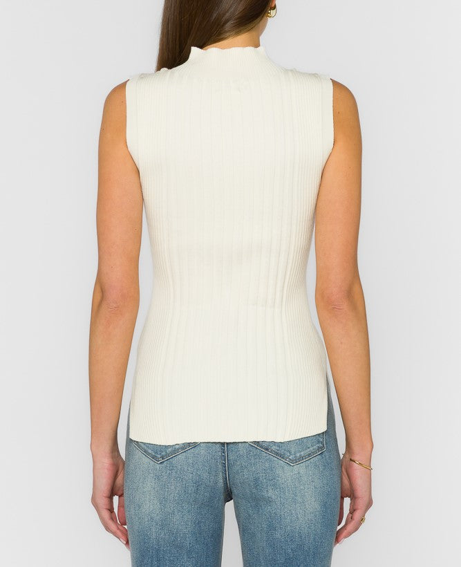 A woman shown from the back wearing a sleeveless, ribbed knit mock neck top in off-white, paired with blue jeans, against a light gray studio background.