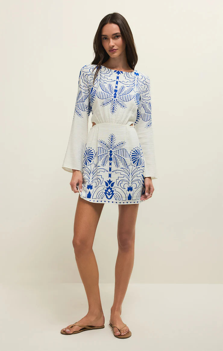 Woman wearing a white dress with blue floral patterns on a plain background