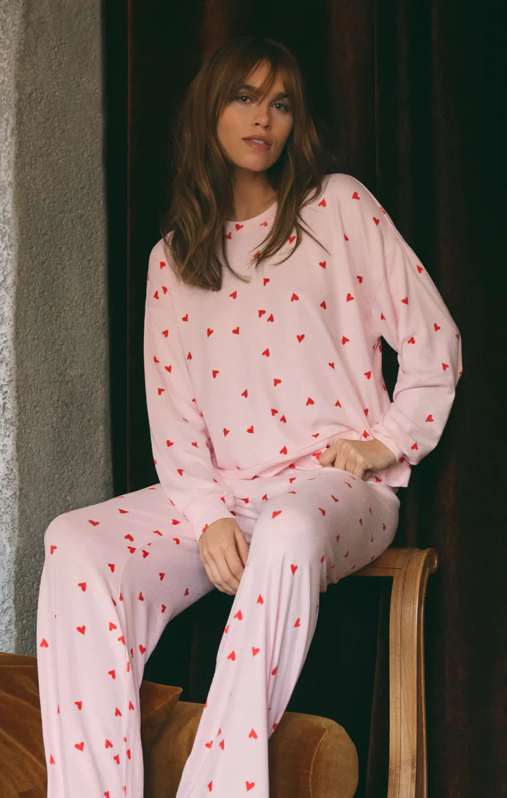 Woman wearing pink pajamas with red heart patterns sitting on a chair.