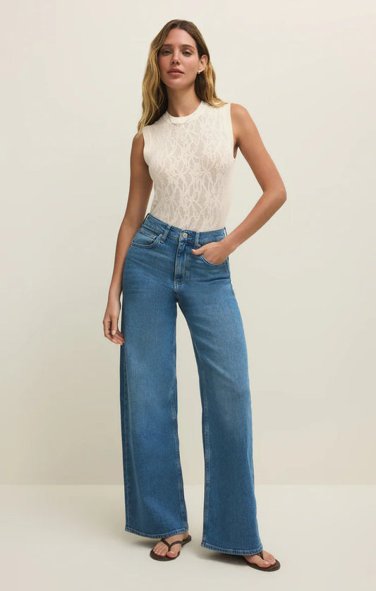 Woman wearing a white sleeveless top and blue jeans on a plain background