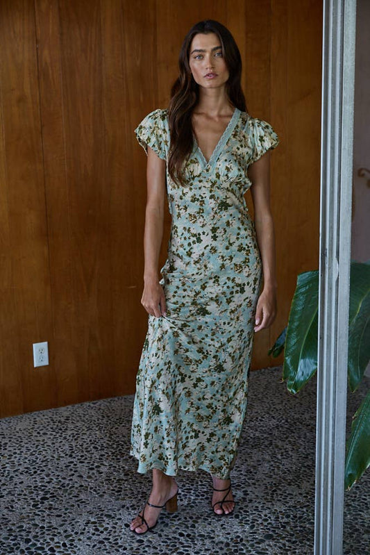 Woman wearing a floral dress standing against a wooden wall.