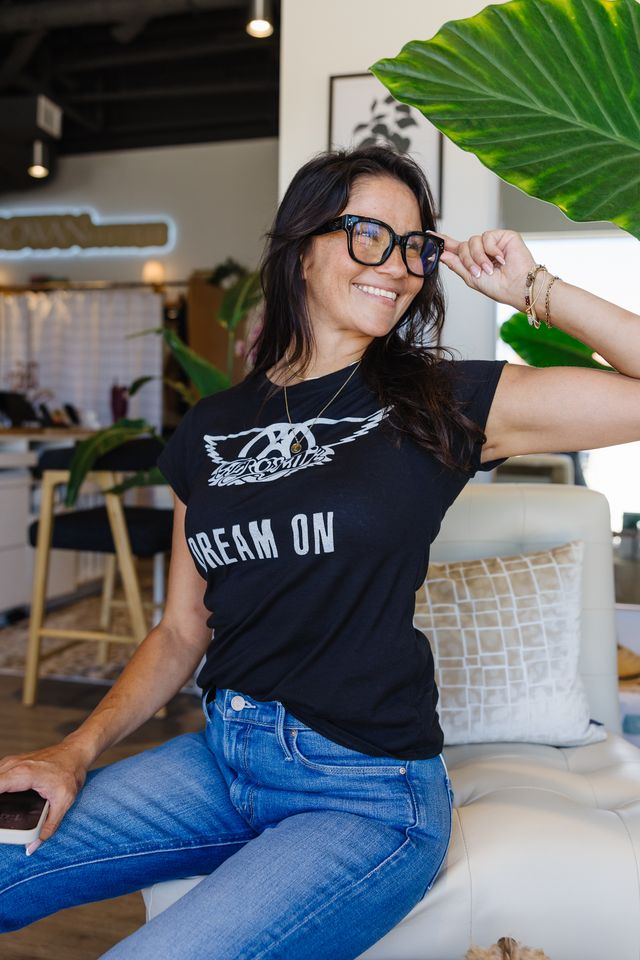 Woman sitting on chair wearing blue jeans and a black shirt that reads "dream on."