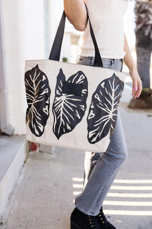 Person holding a tote bag with leaf designs on a sidewalk
