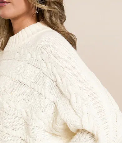 Close-up of a person wearing a white cable knit sweater against a neutral background