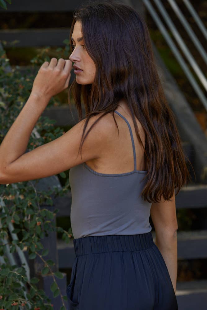 Woman wearing a gray tank top and dark pants outdoors