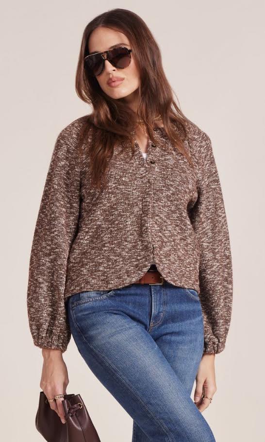 Woman in brown textured cardigan, blue jeans, sunglasses and a clutch bag on a white background.