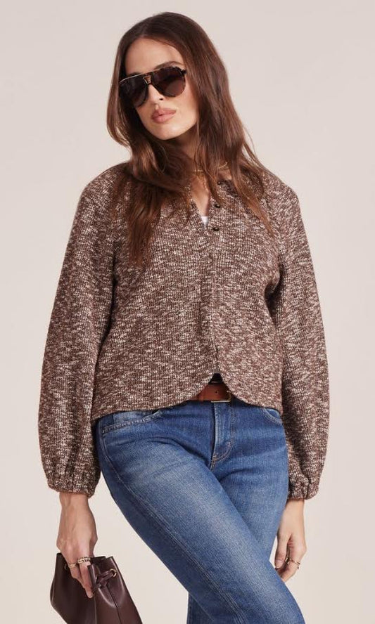 Woman in brown textured cardigan, blue jeans, sunglasses and a clutch bag on a white background.