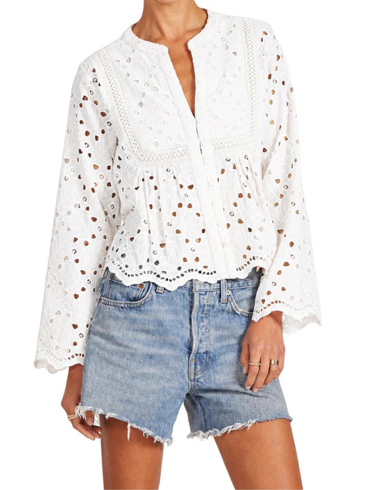 Woman wearing lace log sleeve top and blue jean shorts on white background.