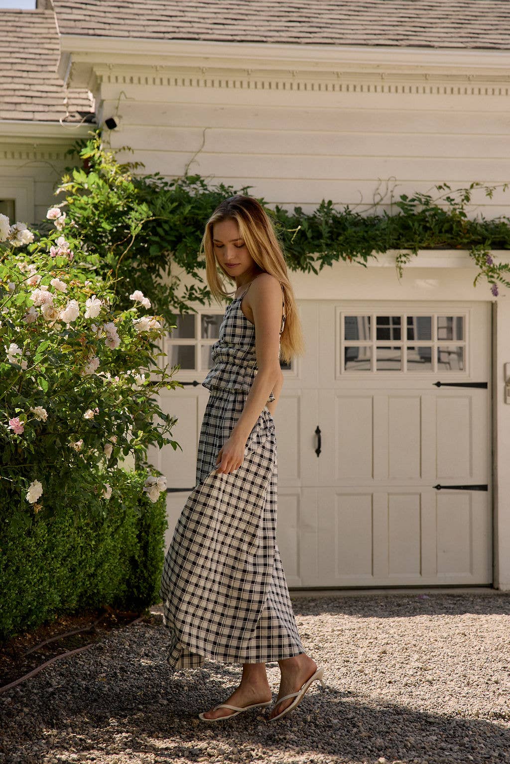 Woman in a checkered dress standing in front of a white building with greenery.