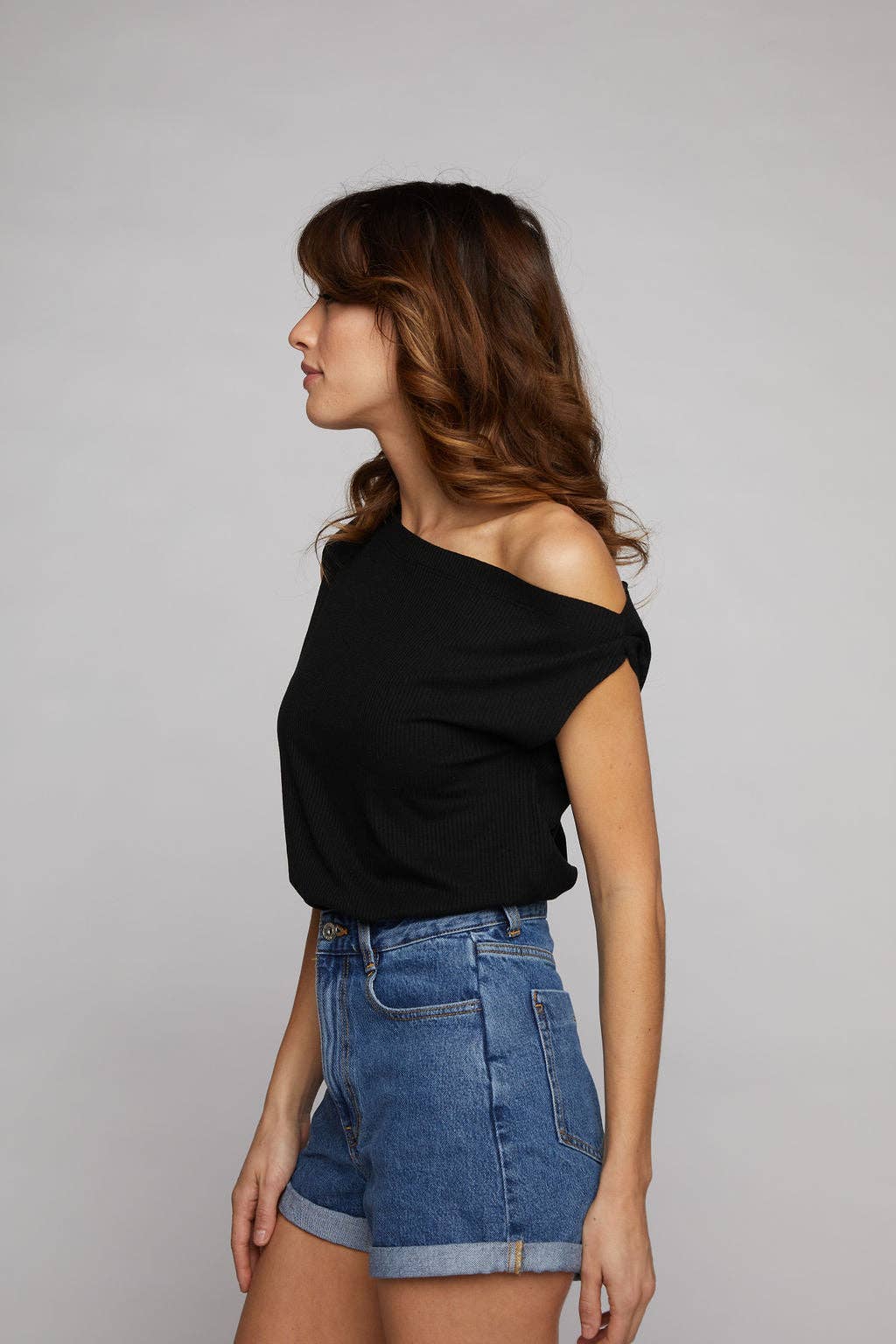 Woman wearing a black top and blue shorts on a gray background