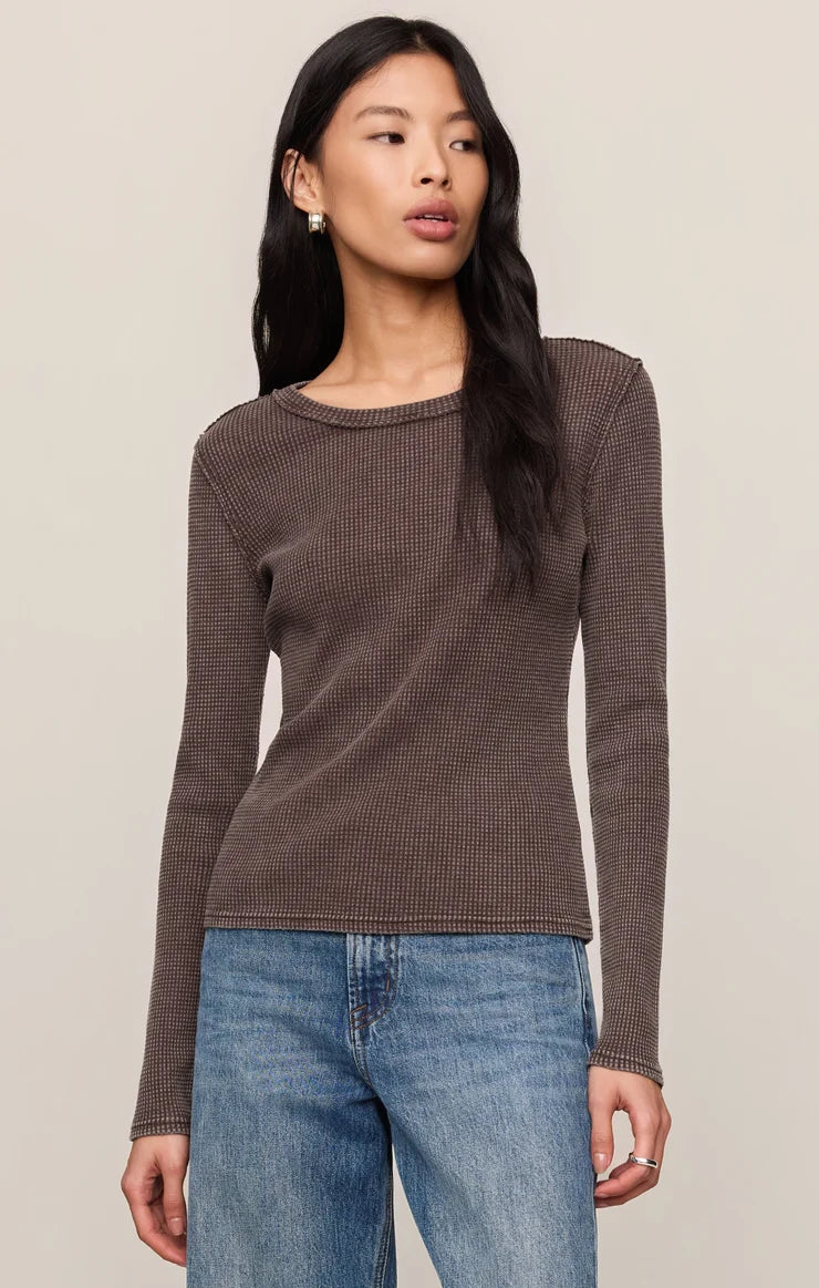 Woman wearing a brown textured long-sleeve top and blue jeans against a beige background