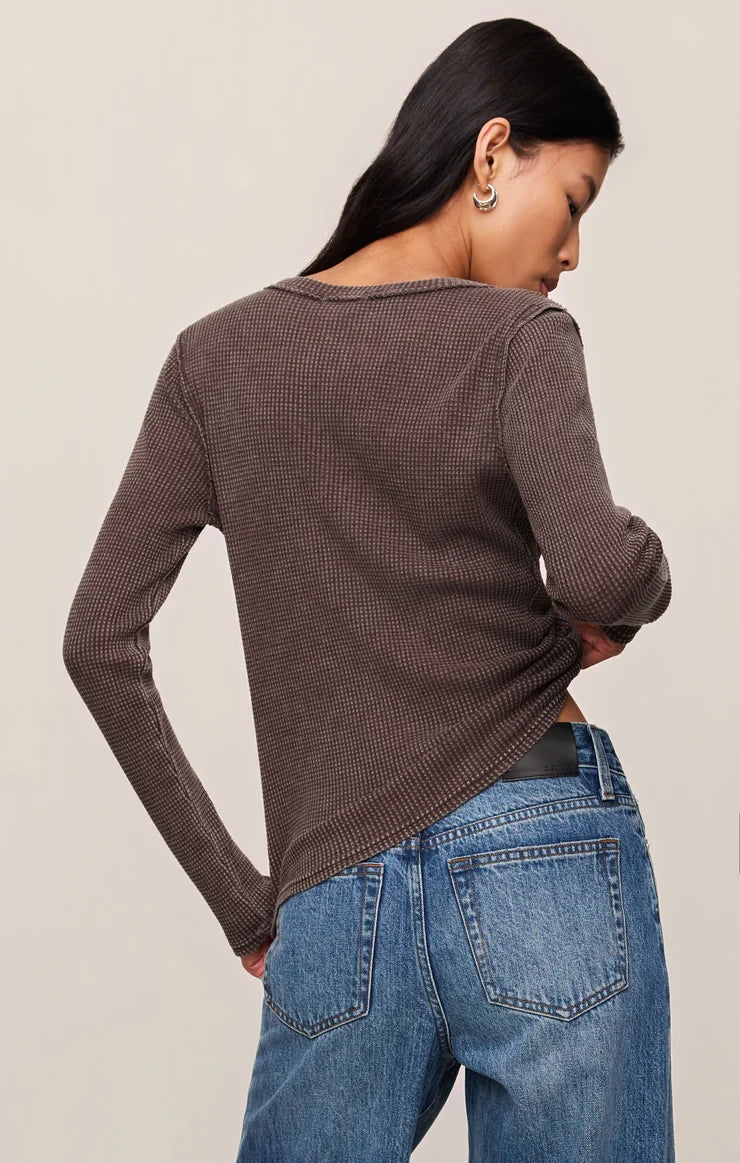 Woman wearing a brown textured long-sleeve top and blue jeans against a beige background