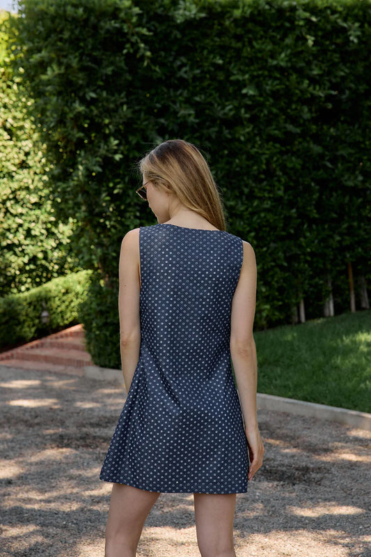 Woman wearing a navy polka dot dress standing outdoors with greenery in the background