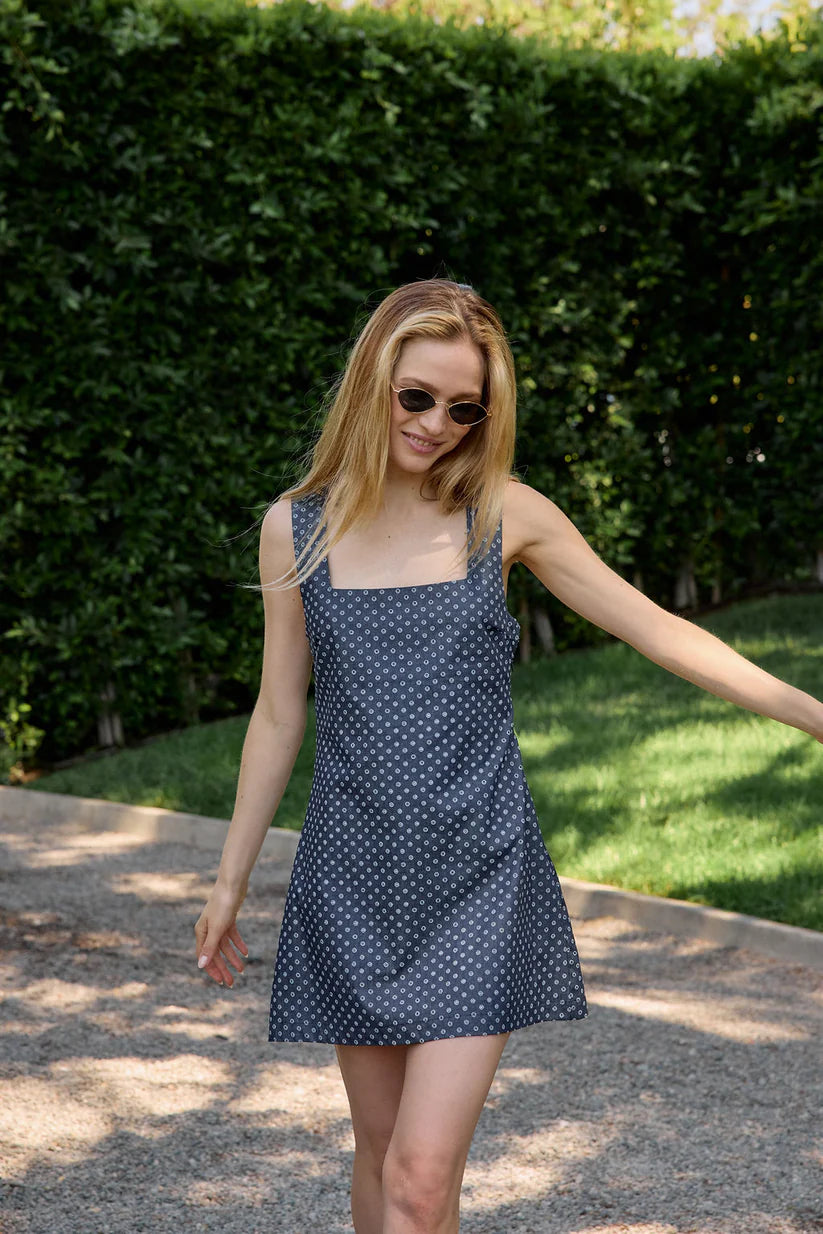 Woman in a polka dot dress standing outdoors with greenery in the background