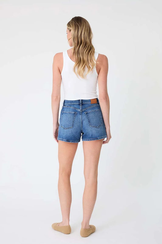 A woman is shown from behind wearing blue denim shorts, a white tank top, and beige flat shoes against a plain white studio background.