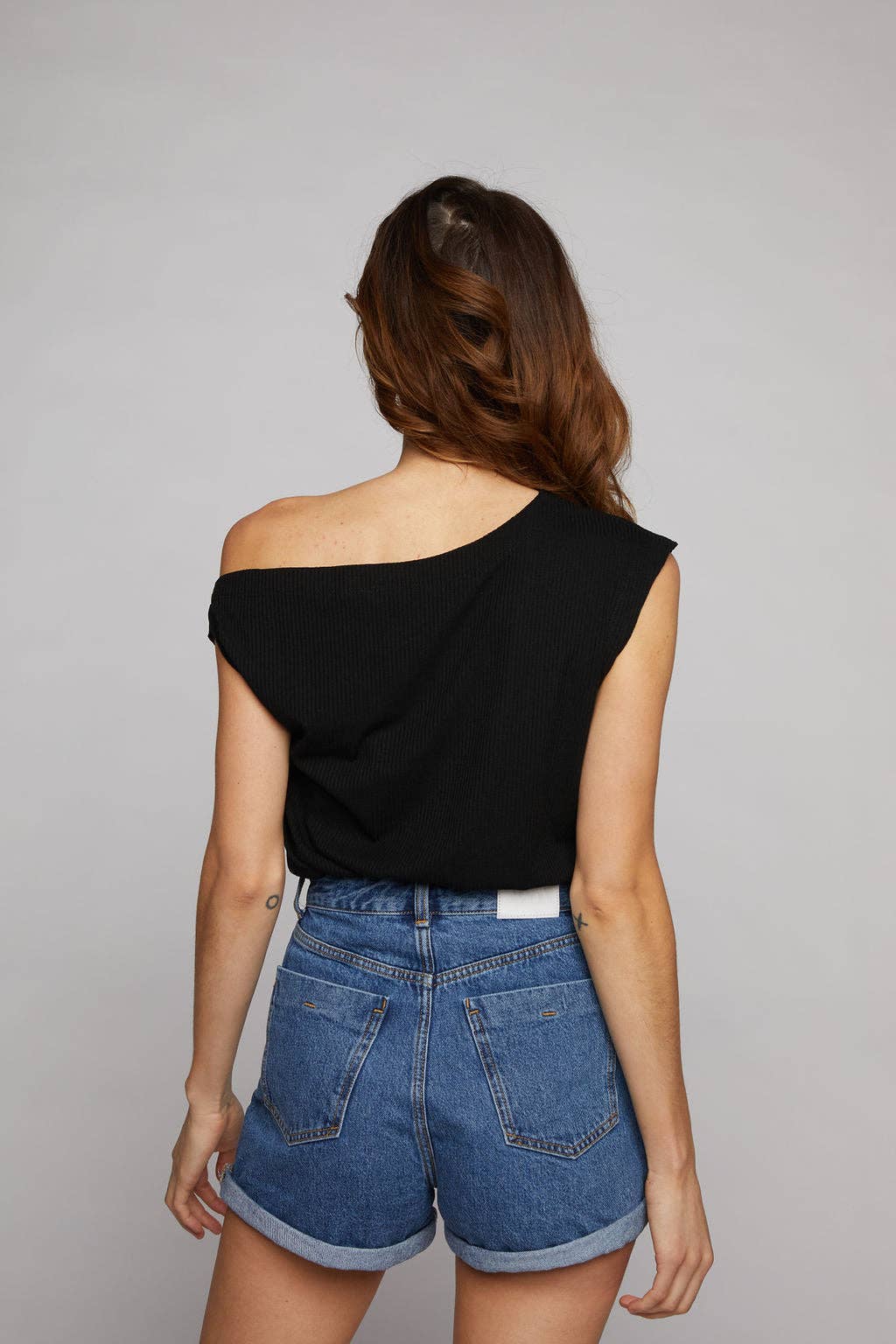 Woman wearing a black one-shoulder top and blue shorts on a gray background