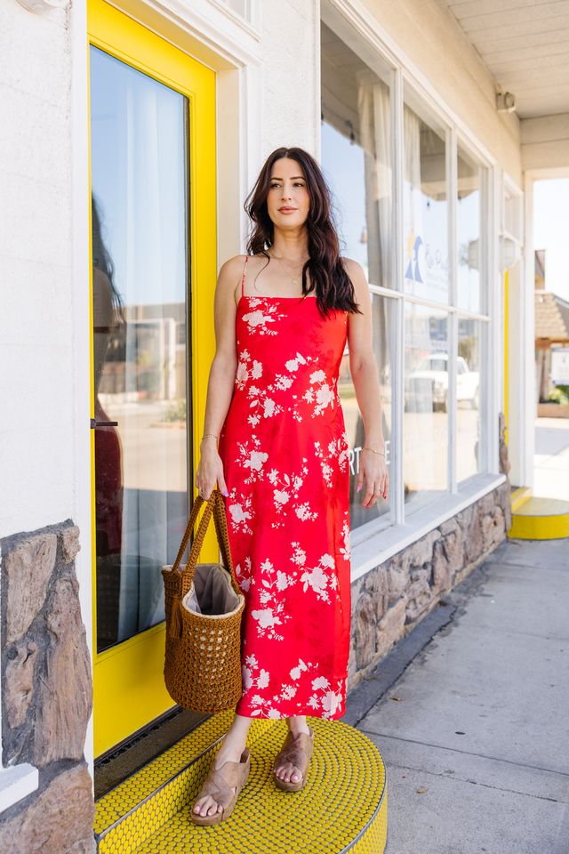 Woman in a red floral dress standing outside a building with yellow door and windows.